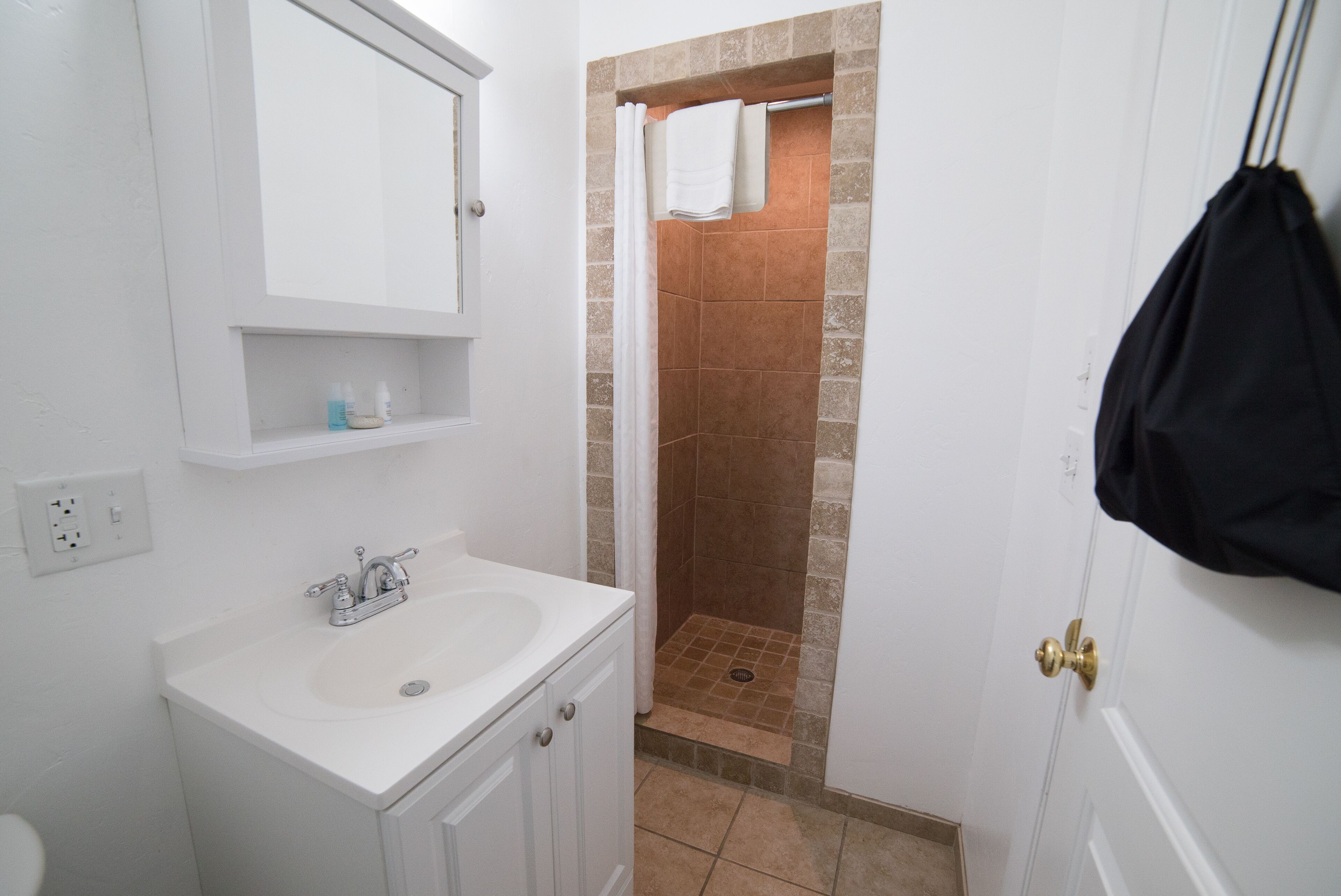 Un baño con lavamanos blanco, un espejo y una ducha con azulejos marrones.