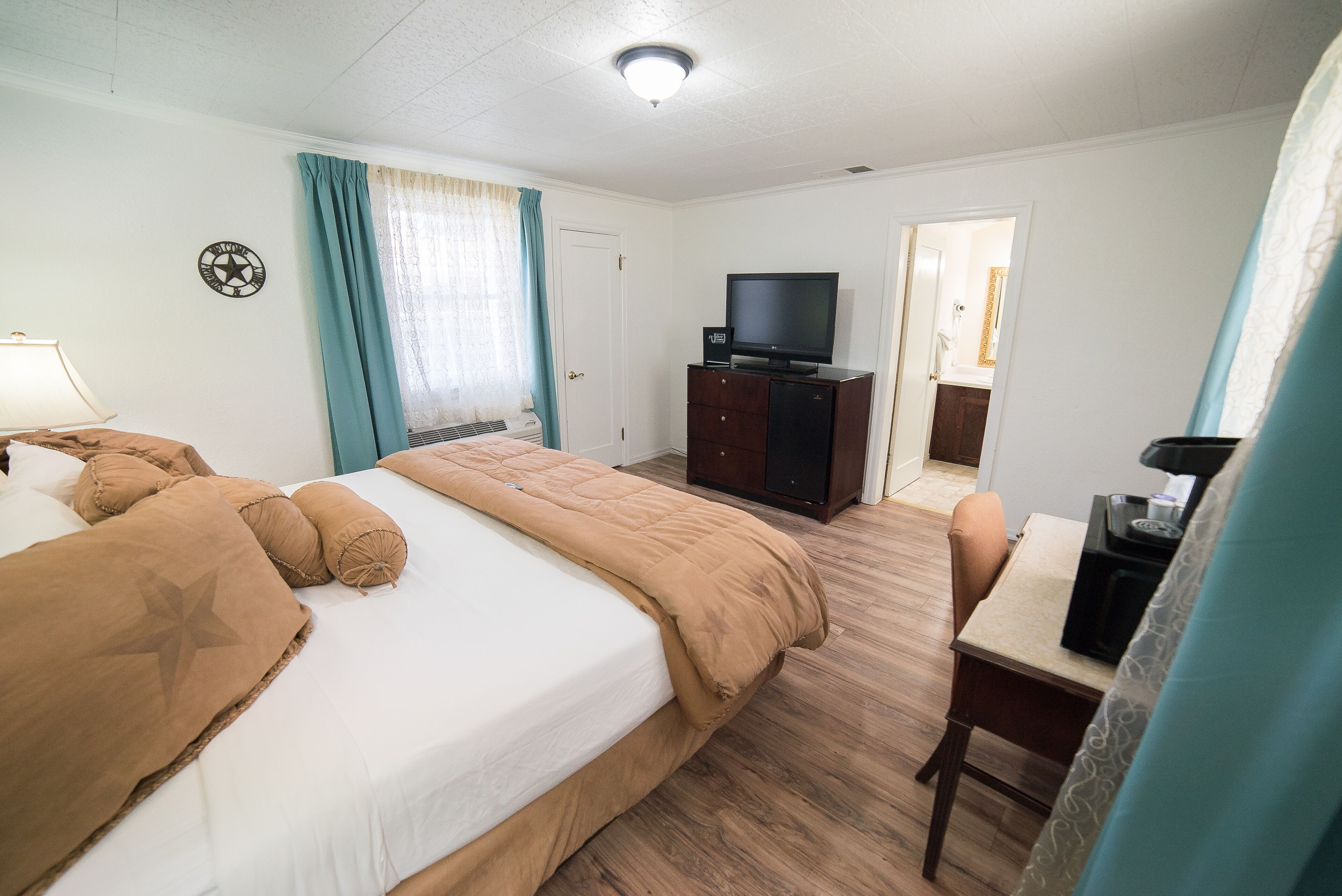 Et hotelværelse med en seng, et skrivebord, et fjernsyn og en dør til et andet rum.