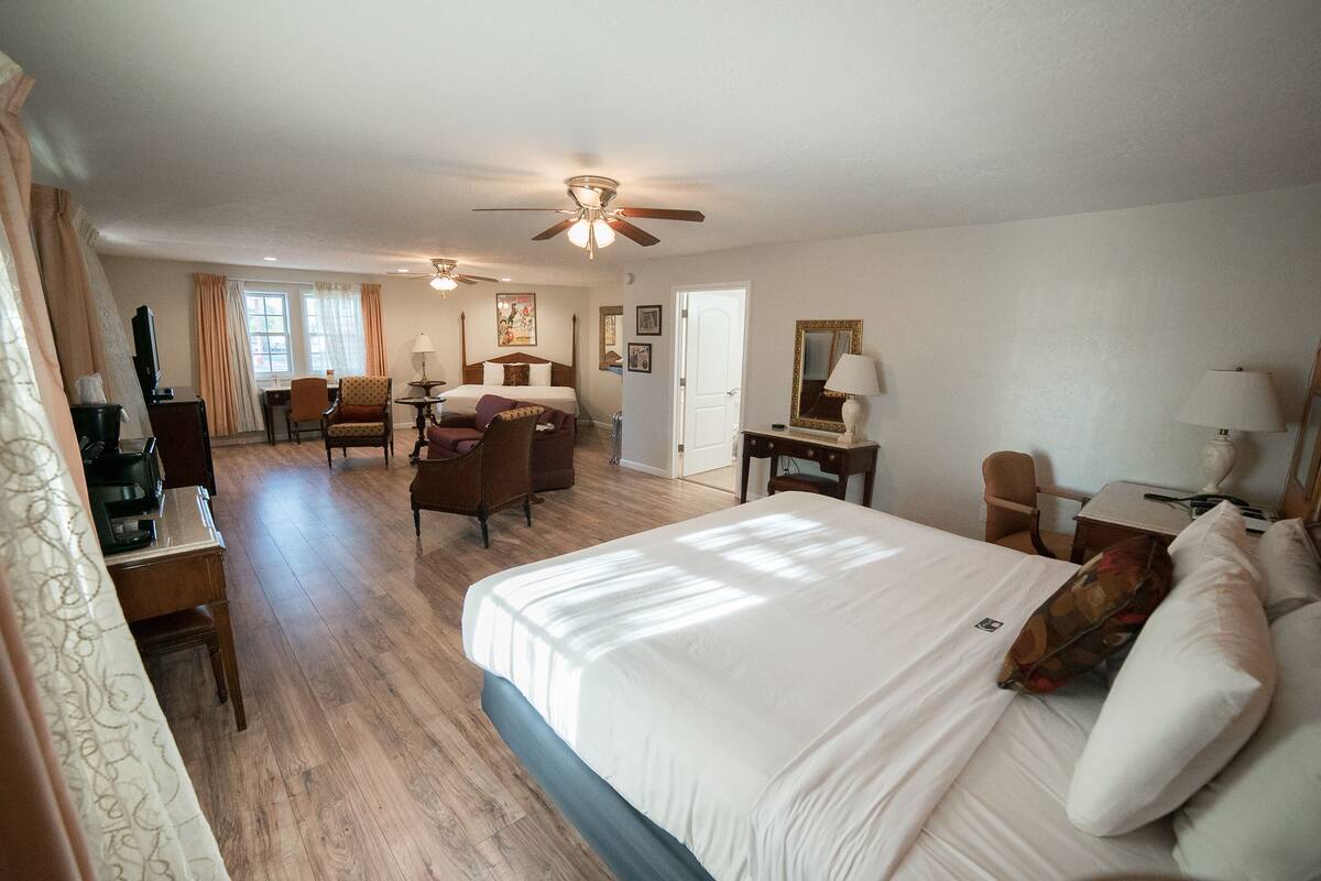 A hotel room with a large bed, a desk with a chair, a small table, and a ceiling fan.