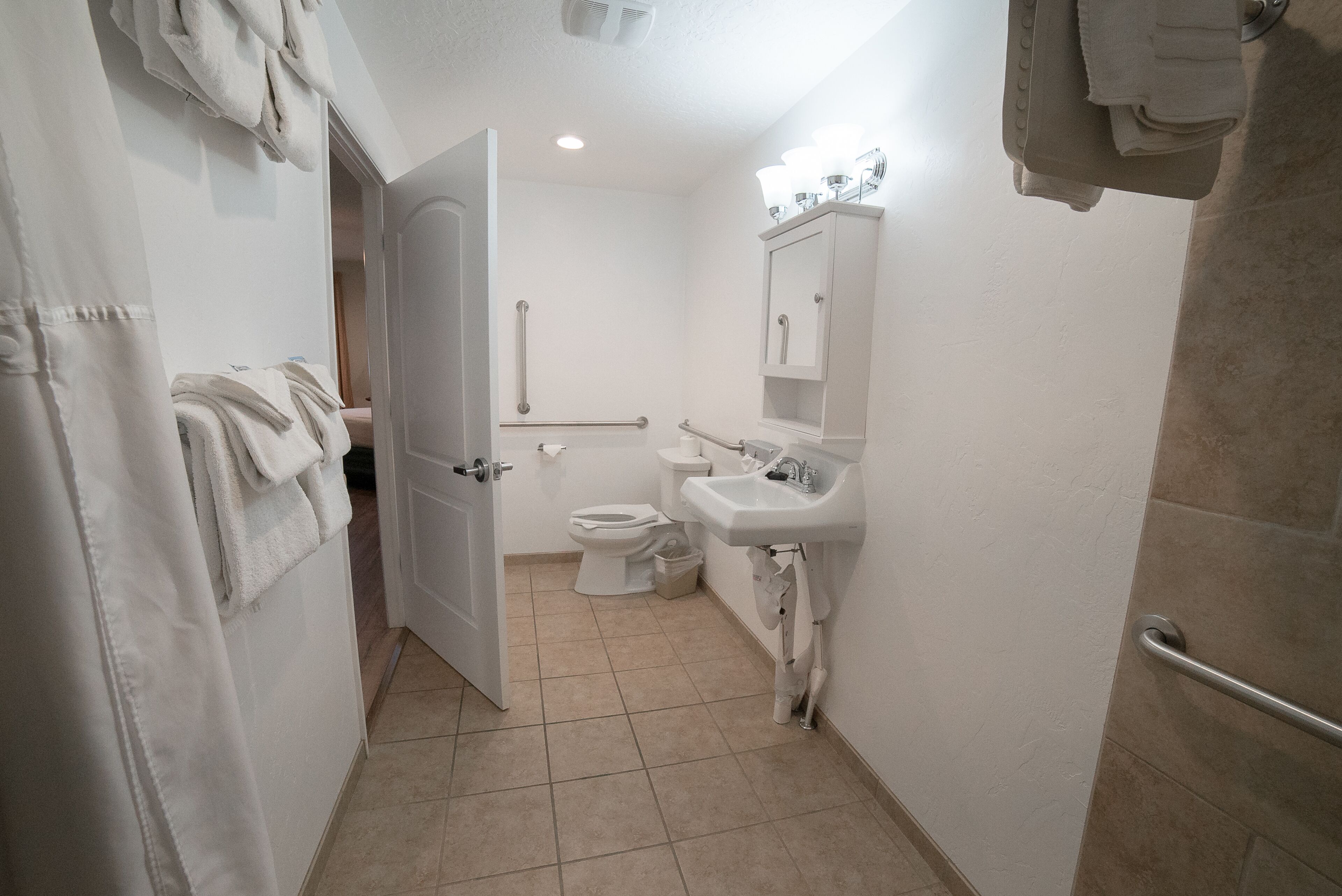 Un baño pequeño y limpio, con inodoro, lavabo y barras de apoyo.