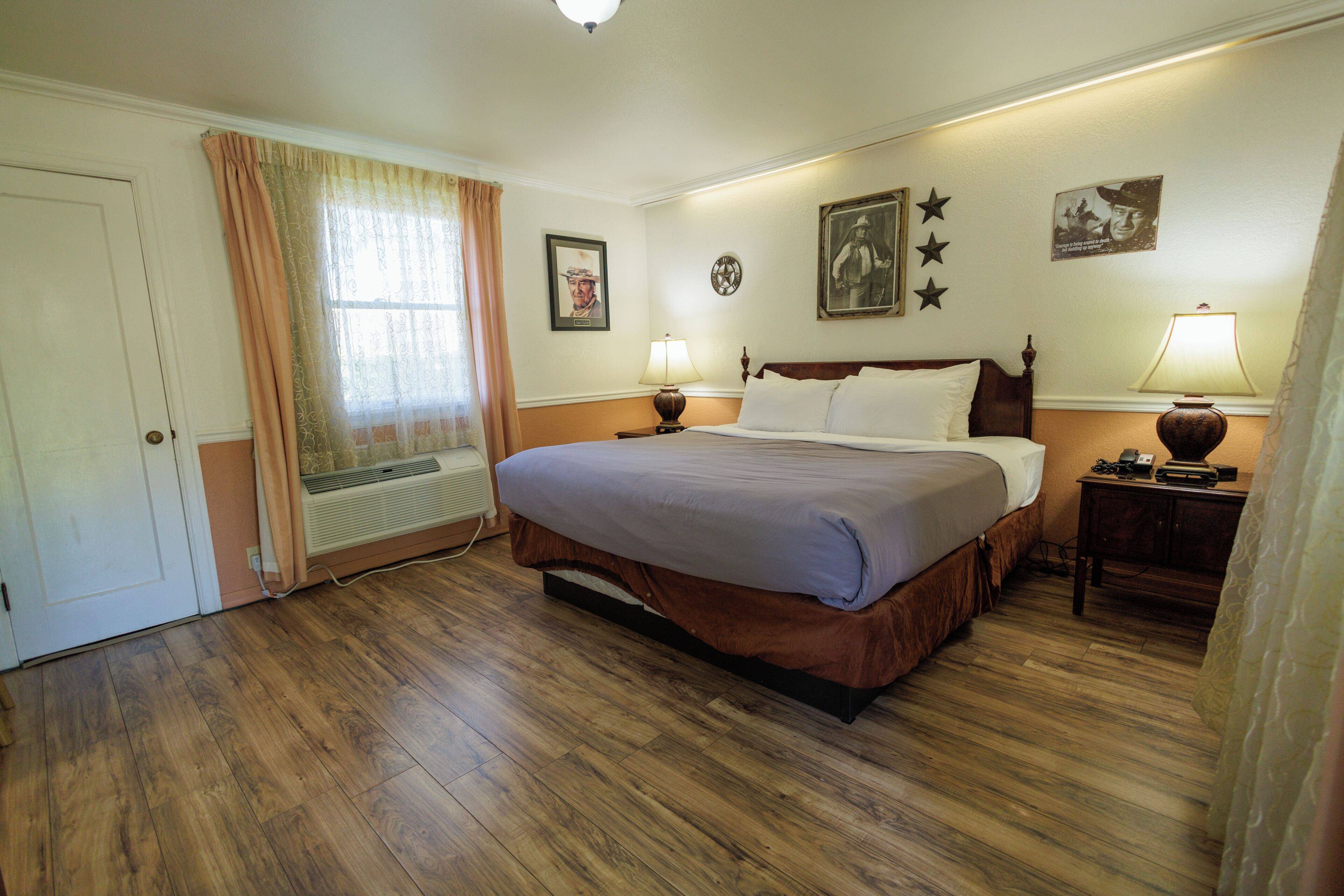 Una habitación de hotel con una cama grande, dos lámparas de noche, un calentador, una ventana con cortinas y decoración en la pared, incluyendo estrellas y cuadros enmarcados.