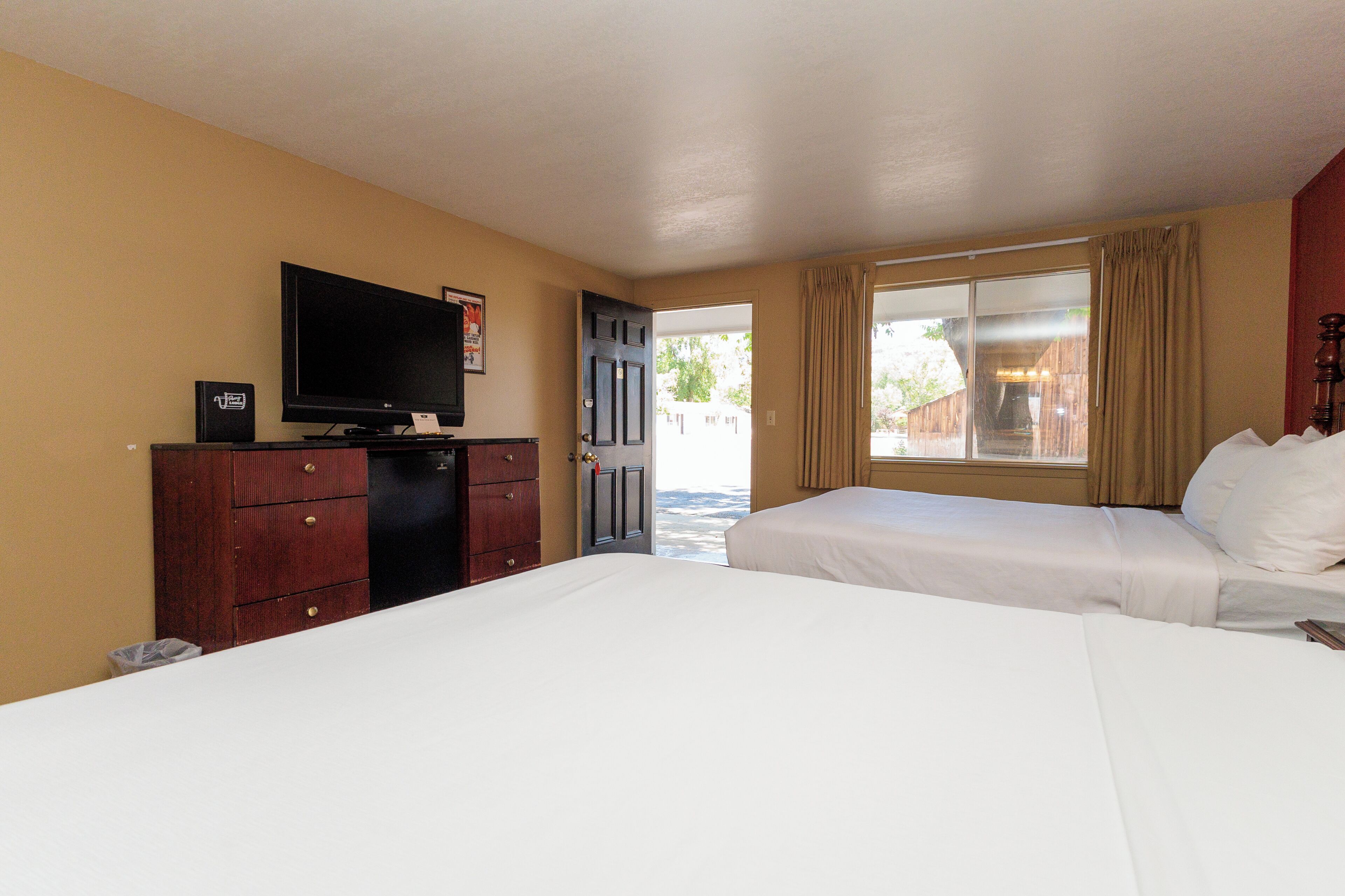 A hotel room with a bed, a TV, a dresser, and a door leading to a balcony.