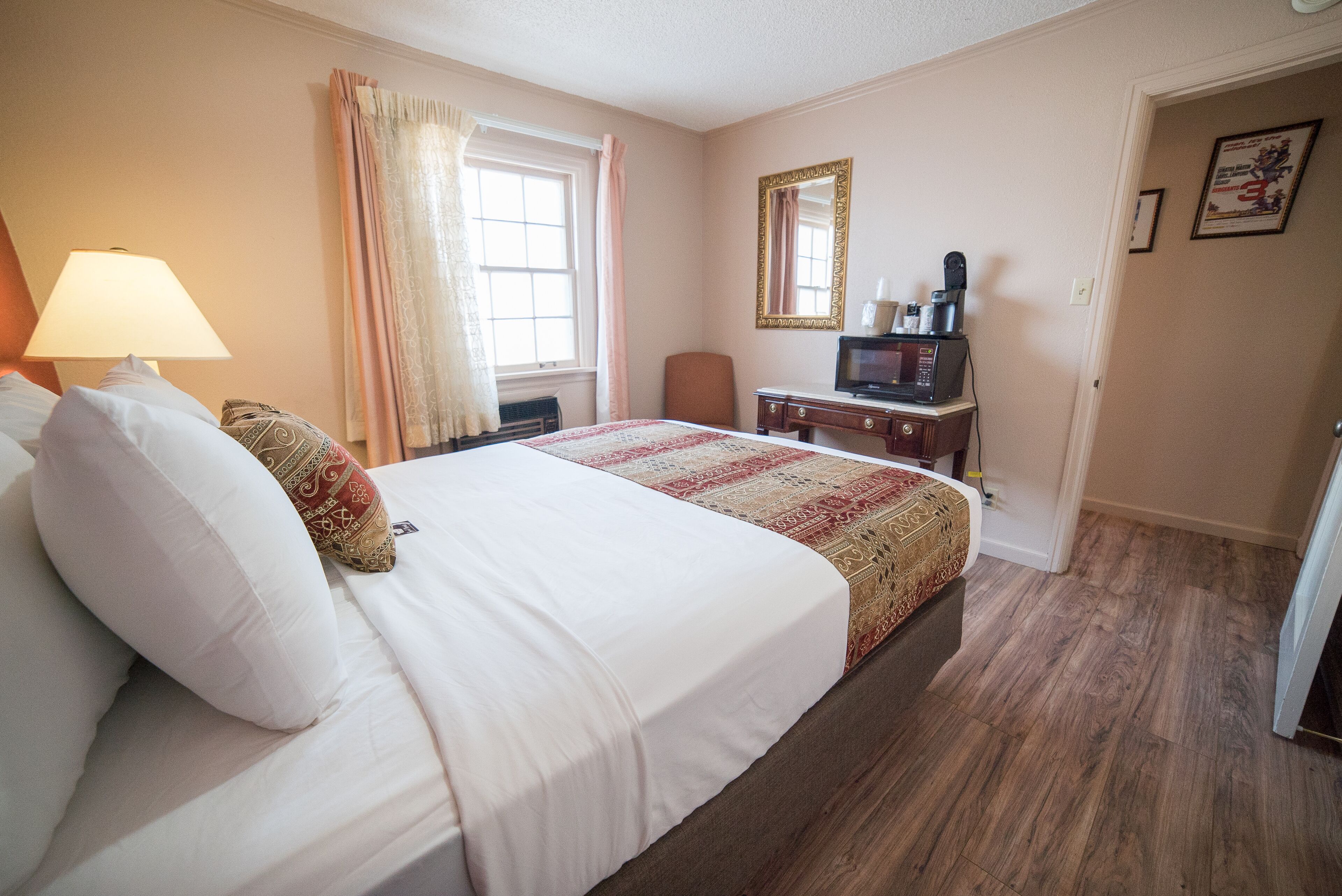 Une chambre d’hôtel avec un grand lit, un bureau avec un ordinateur, une chaise, une fenêtre avec des rideaux et une porte.