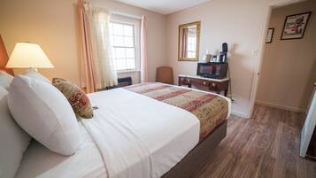 Une chambre d’hôtel avec un grand lit, un bureau avec un ordinateur, une chaise, une fenêtre avec des rideaux et une porte.