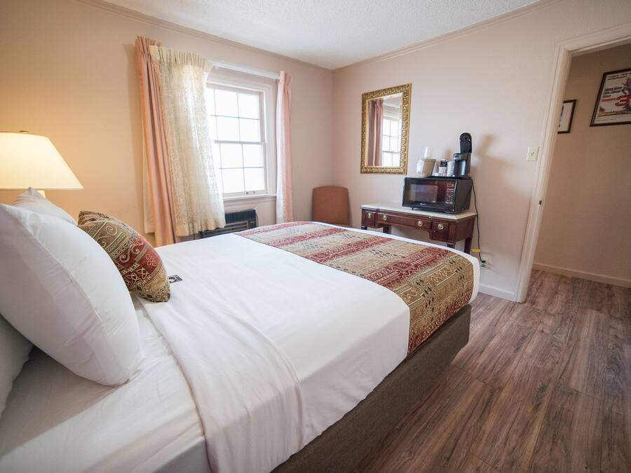 Une chambre d’hôtel avec un grand lit, un bureau avec un ordinateur, une chaise, une fenêtre avec des rideaux et une porte.