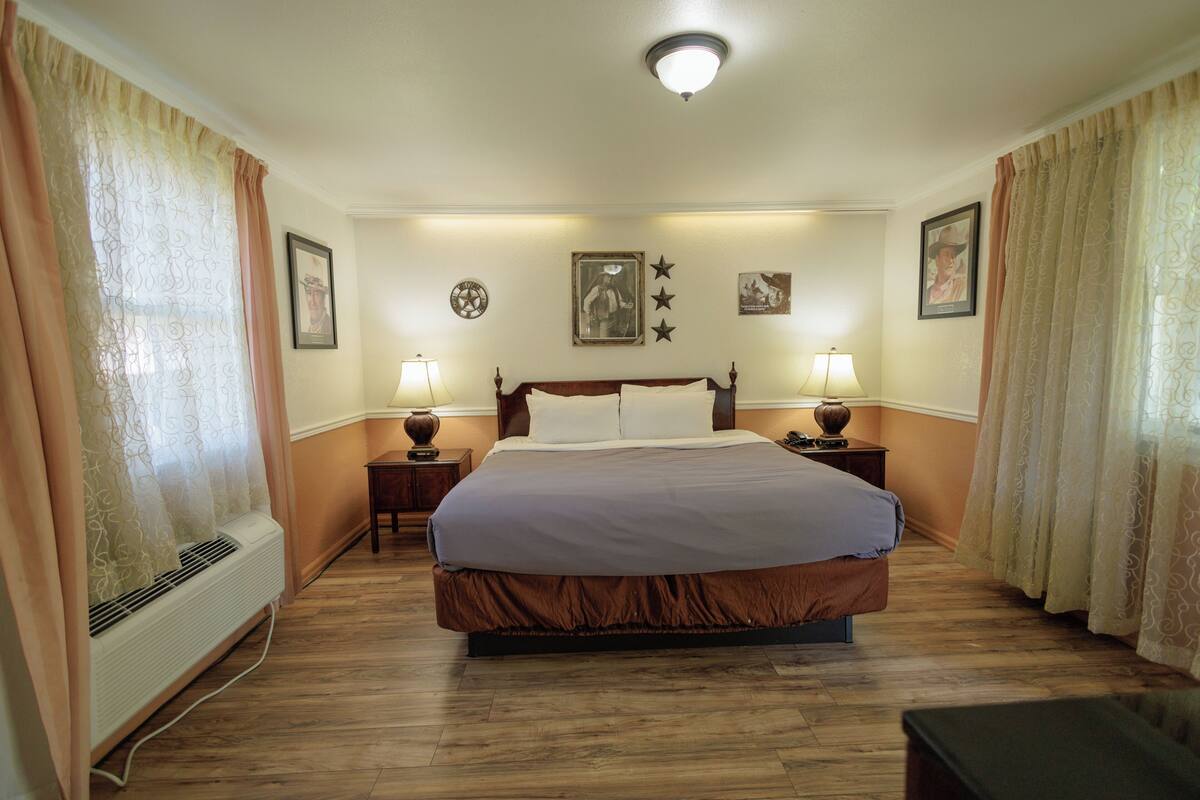 A hotel room with a large bed, two bedside tables with lamps, a wall clock, and a ceiling light.