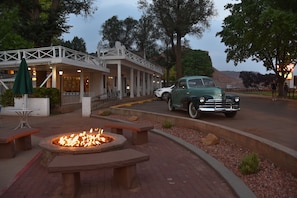 Un bâtiment historique doté d’un porche couvert, d’un foyer extérieur et d’une voiture ancienne garée devant.