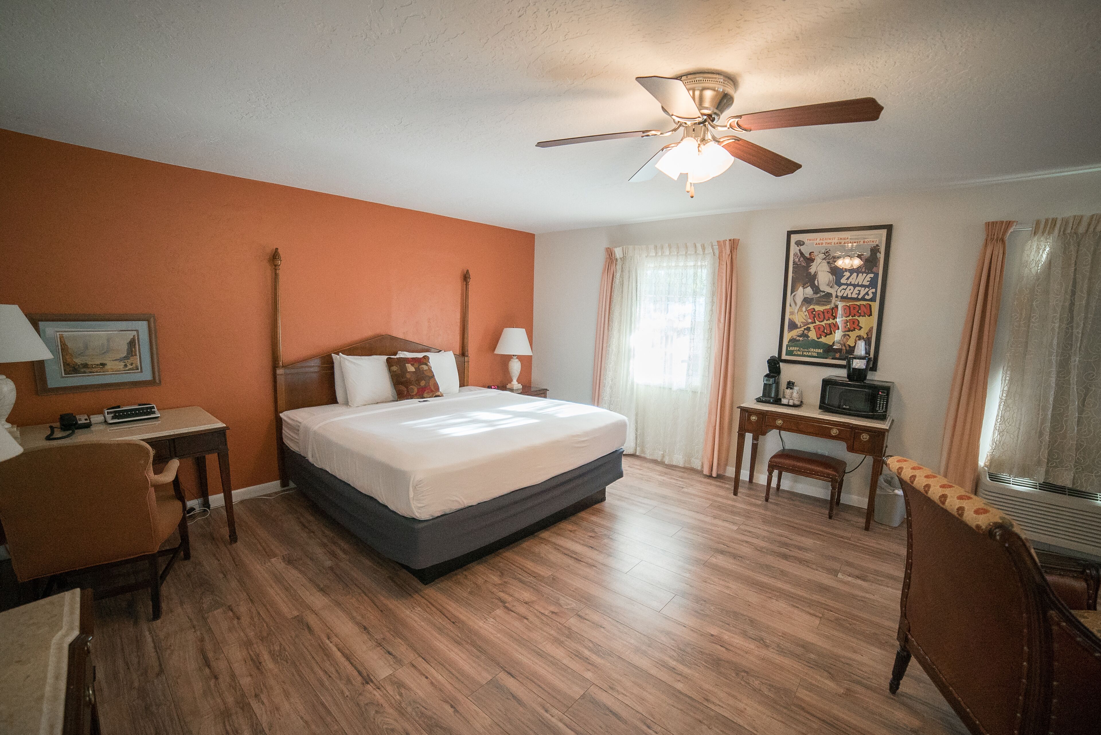 A hotel room with a bed, desk, chair, and a ceiling fan.