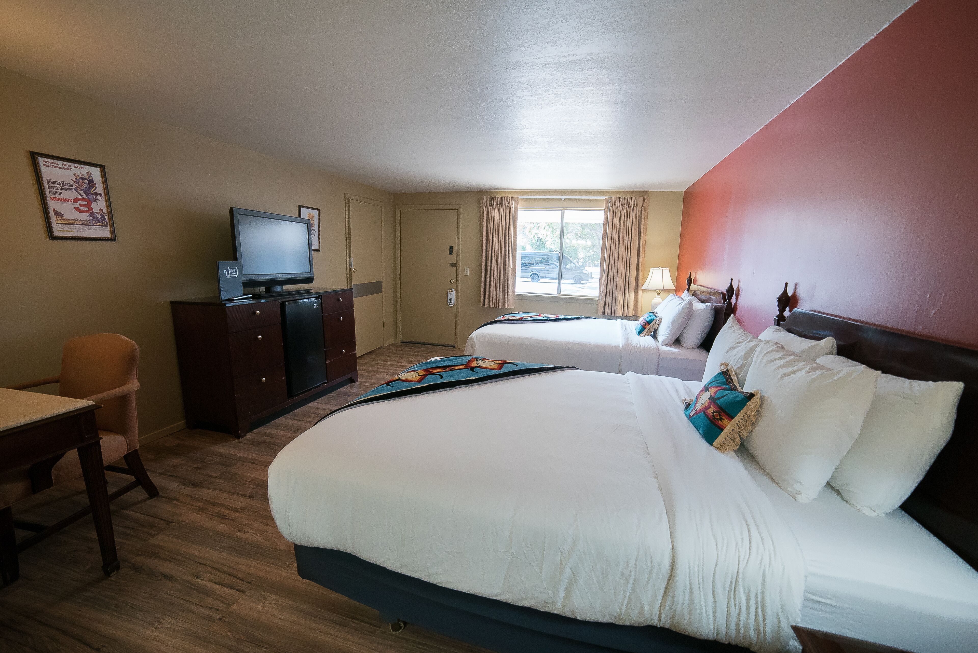 A hotel room with a large bed, a desk, a television, and a window with curtains.