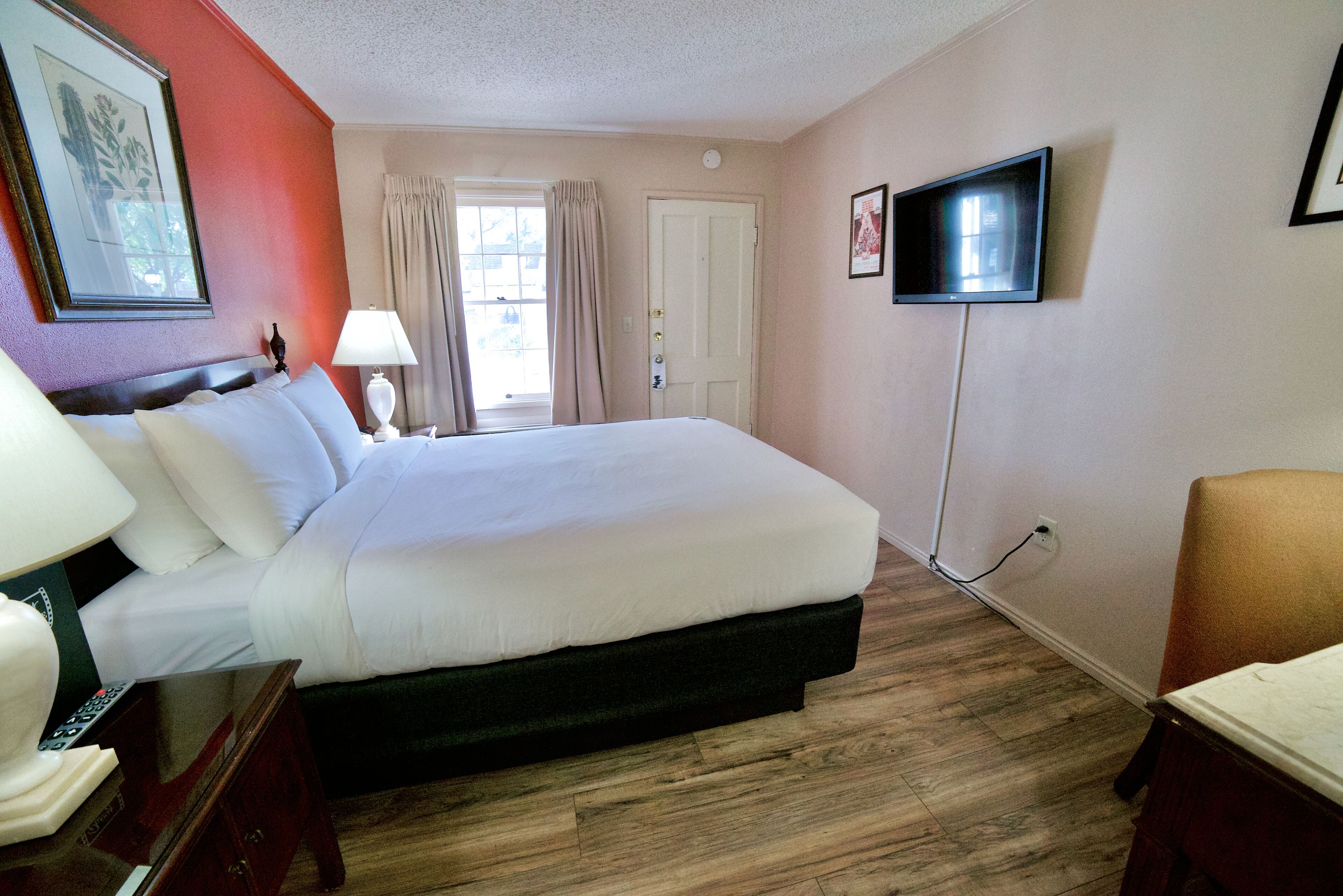 A hotel room with a large bed, a television mounted on the wall, and a window with curtains.