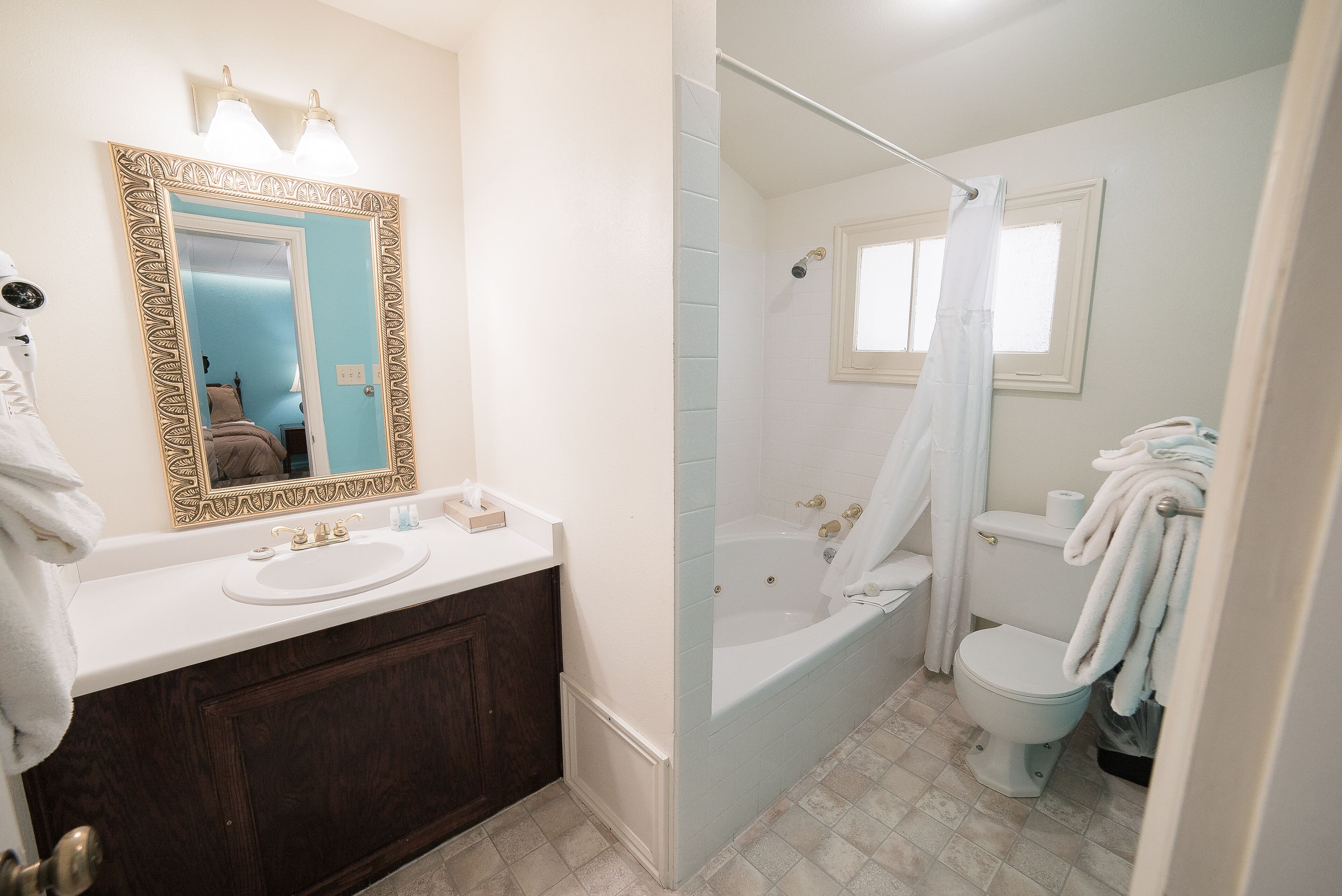 A bathroom with a white sink, dark wooden vanity, a large mirror with decorative frame, a bathtub, and a white toilet.