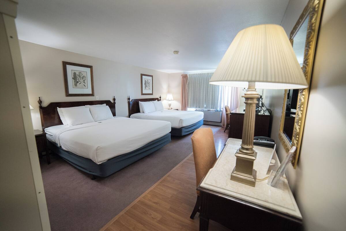 A hotel room with two beds, a desk, a lamp, and a mirror.