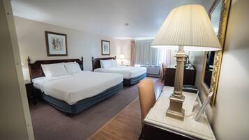 A hotel room with two beds, a desk with a lamp, and a mirror.