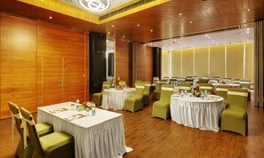 Uma sala de conferências com mesas redondas, cadeiras verdes e toalhas de mesa brancas.