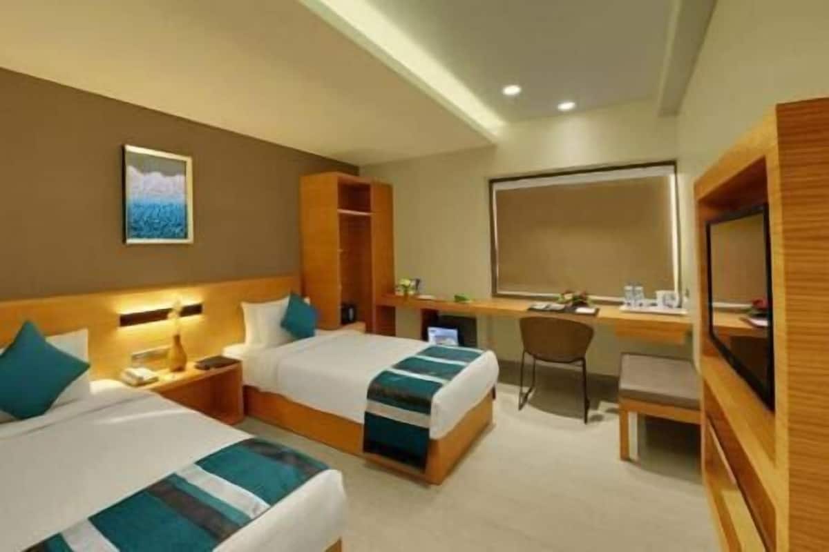 A hotel room with two beds, a desk, a chair, a mirror, and a painting on the wall.