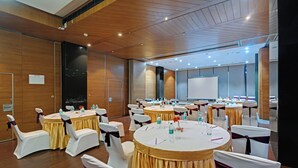 A conference room with multiple round tables, white chairs with purple sashes, and a large projection screen. - Hotel Suba Elite Vadodara (Vadodara)