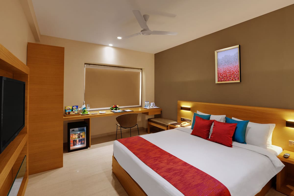 A hotel room with a bed, bedside table, nightstand, desk, chair, and a television.