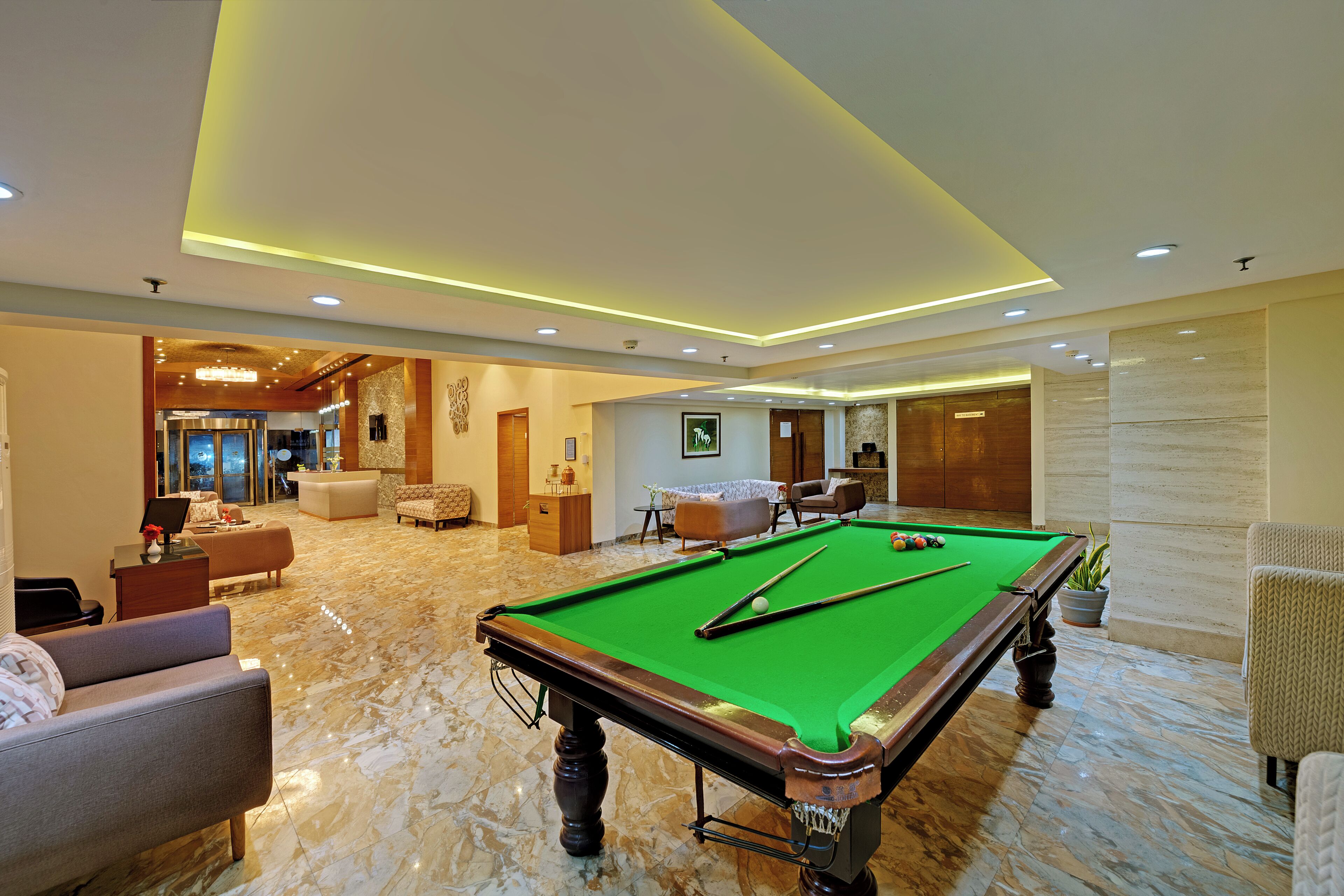 A pool table in a well-lit room with a marble floor, surrounded by comfortable seating and a reception area.