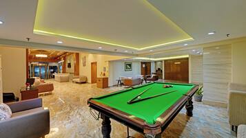 A pool table in a well-lit room with a marble floor, surrounded by comfortable seating and a reception area.