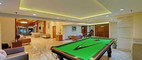 A pool table in a well-lit room with a marble floor, surrounded by comfortable seating and a reception area.