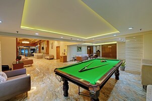 A pool table in a well-lit room with a marble floor, surrounded by comfortable seating and a reception area.