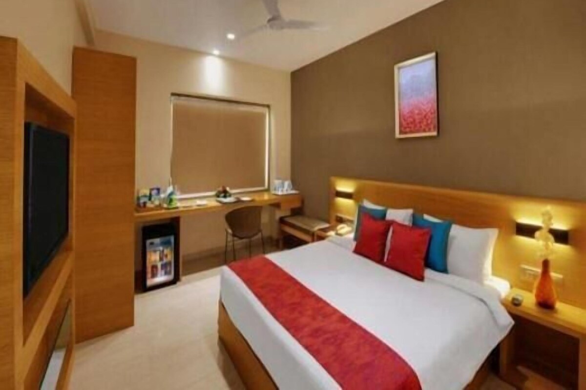 Una habitación de hotel con cama, escritorio, silla, televisor y ventilador de techo.
