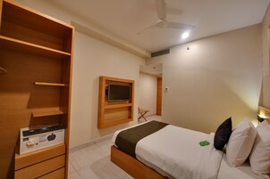 A bedroom with a bed, a TV mounted on the wall, a wardrobe, and a ceiling fan.
