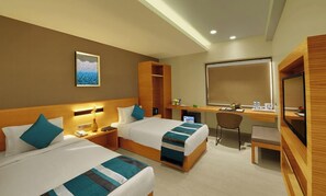 Quarto de hotel com duas camas, uma escrivaninha, uma cadeira, um espelho e um quadro na parede.