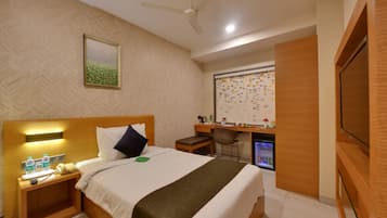 A hotel room with a bed, bedside table, desk, chair, and a television.
