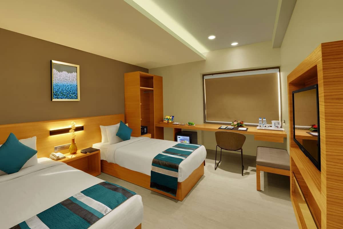 A hotel room with two beds, a desk, a chair, a mirror, and a small TV.