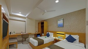 A hotel room with two beds, a desk, a chair, a television, and a ceiling fan. - Hotel Suba Elite Vadodara (Vadodara)