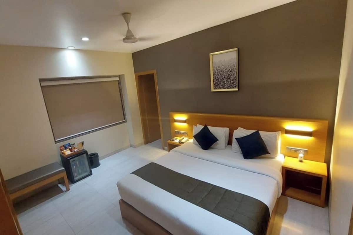 A hotel room with a large bed, bedside tables, a ceiling fan, a wall-mounted artwork, and a window with a blind.