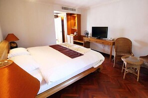 Una habitación de hotel con una cama grande, un escritorio con televisor, una silla y una lámpara.