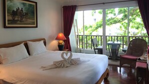 A hotel room with a bed, a painting on the wall, a balcony with a table and chairs, and a window with curtains. - Chada Thai House (Pattaya)