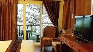 Habitación de hotel con cama, televisión, silla y balcón con vistas a árboles.