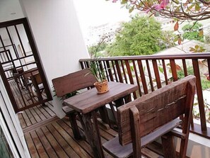 A wooden deck with a bench and a table, a potted plant, and a view of greenery. - Chada Thai House (Pattaya)
