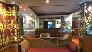 A room with a wicker sofa, wooden chairs, and a patterned wall. - Chada Thai House (Pattaya)