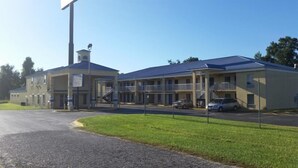 Un motel composé d’un bâtiment à deux étages, d’une entrée principale abritée et d’un parking où sont stationnées plusieurs voitures.