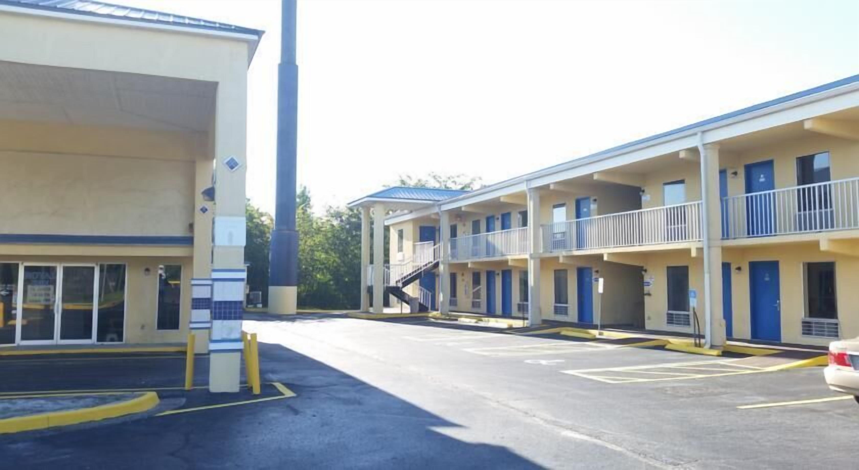 Een motel met een parkeerplaats, meerdere kamers en een trap naar de bovenverdieping.
