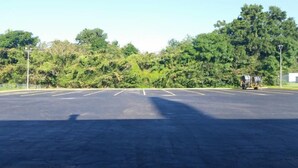 Un grand parking vide, avec des emplacements de stationnement délimités et quelques arbres en arrière-plan.