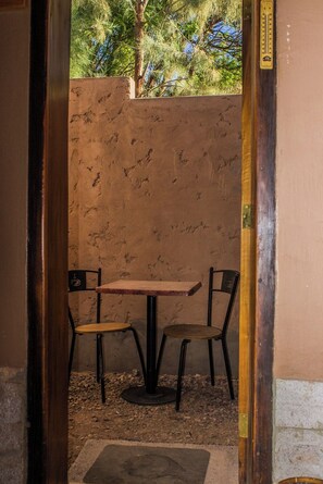 Uma pequena área externa com mesa e duas cadeiras, parede texturizada e moldura de porta de madeira.