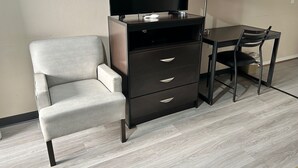 A room with a desk, chair, TV, and storage unit. - The Surrey Inn (Caldwell)