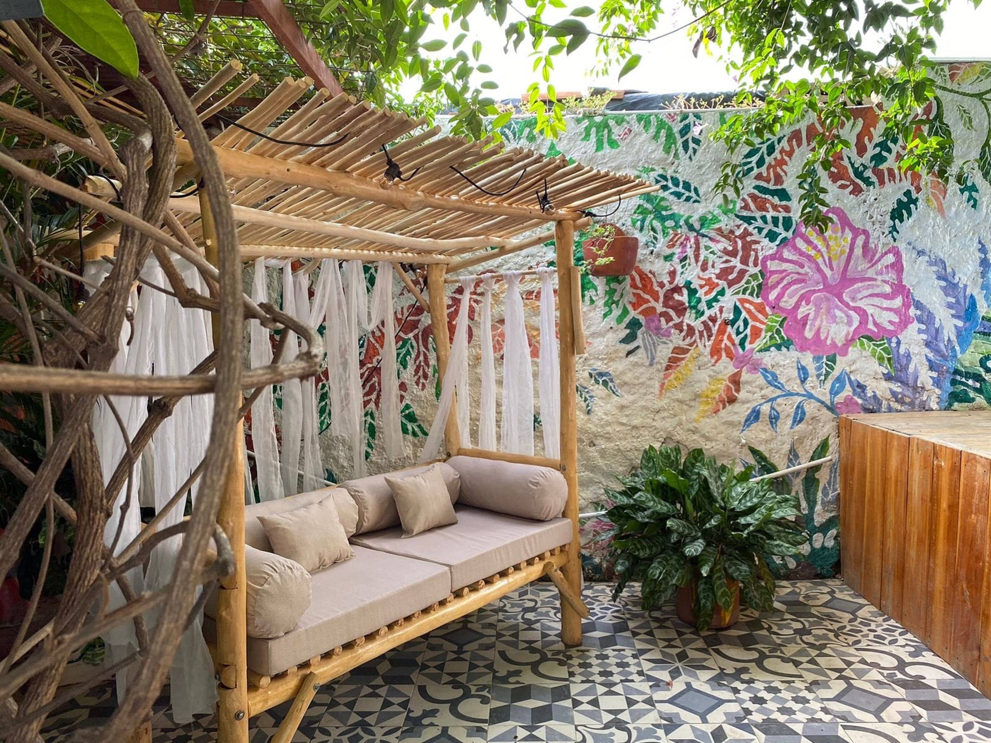 Un área de descanso tipo hamaca con un banco acolchado, rodeada por una pérgola de madera y un mural colorido.