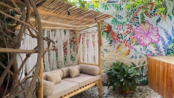 Un área de descanso tipo hamaca con un banco acolchado, rodeada por una pérgola de madera y un mural colorido.