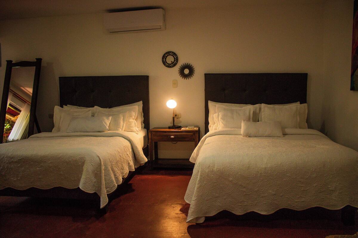 A hotel room with two single beds, a nightstand with a lamp, a wall-mounted mirror, and a decorative plate.