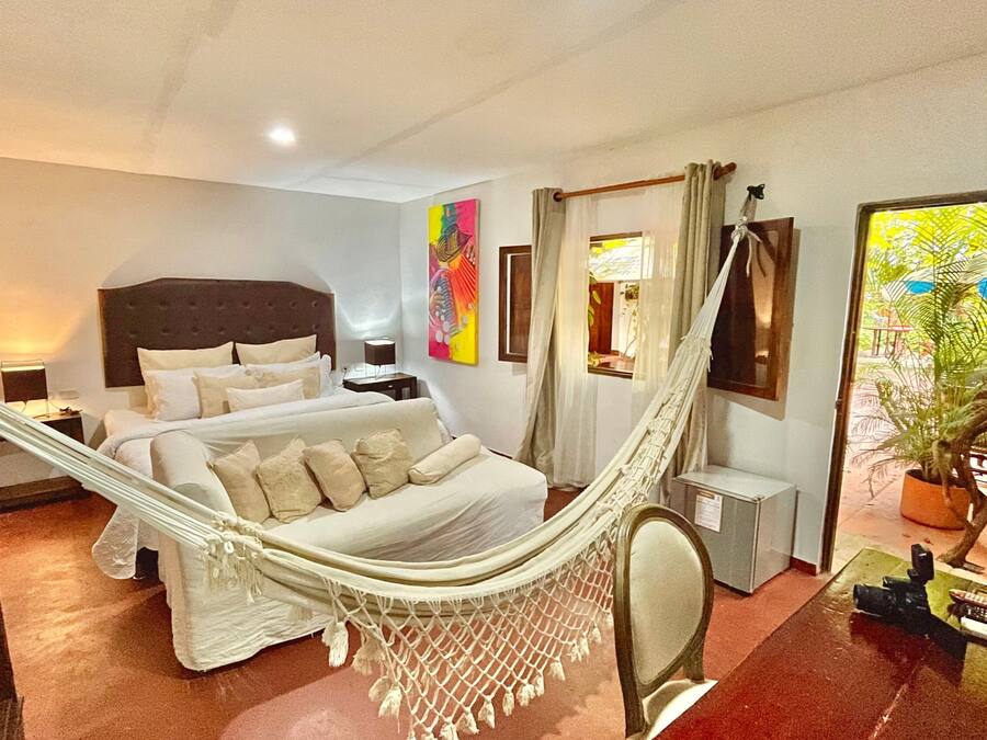 Een slaapkamer met een bed, een hangmat, een bureau, een stoel en een potplant.