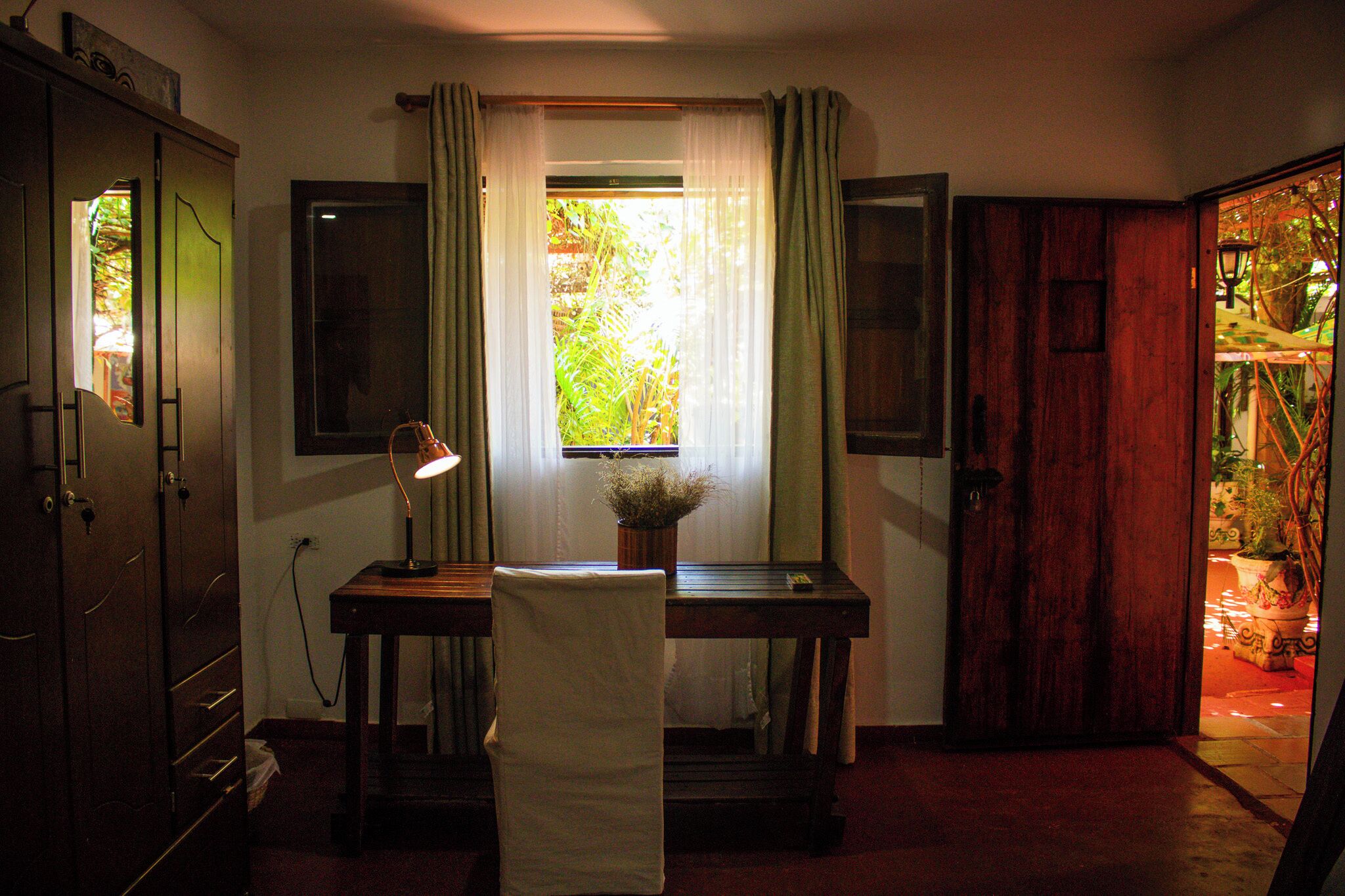 A room with a desk, chair, lamp, and a window with curtains.