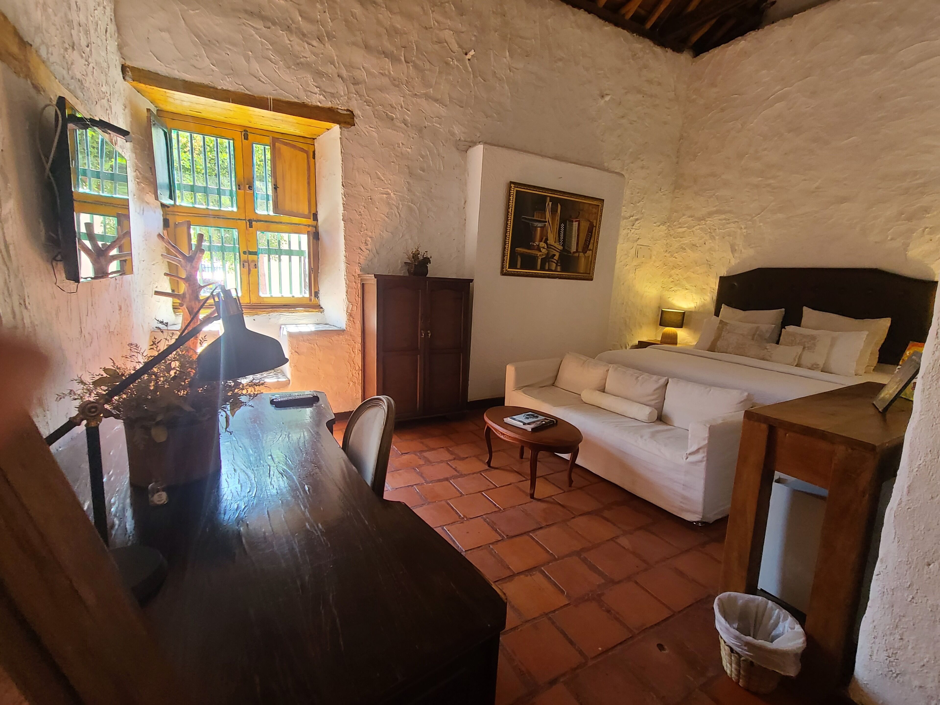 Una habitación acogedora con un escritorio de madera, un sofá blanco, una cama y una ventana con vistas a la vegetación.