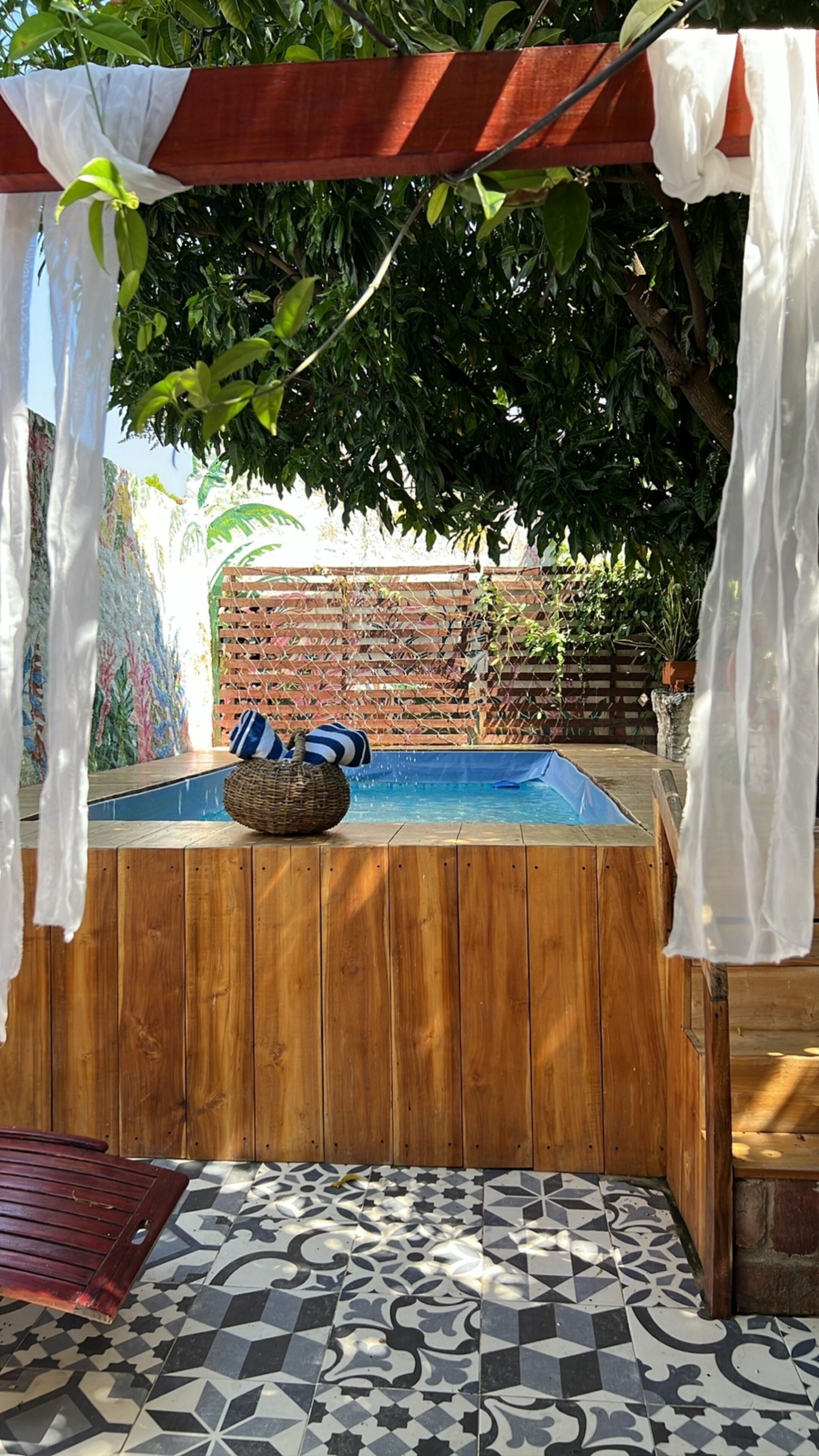 A wooden hot tub with a tiled floor, surrounded by a wooden fence and covered by a white canopy.