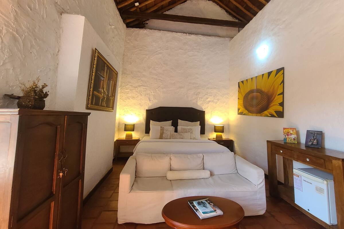 A cozy room with a bed, a sofa, a small table, and a refrigerator.